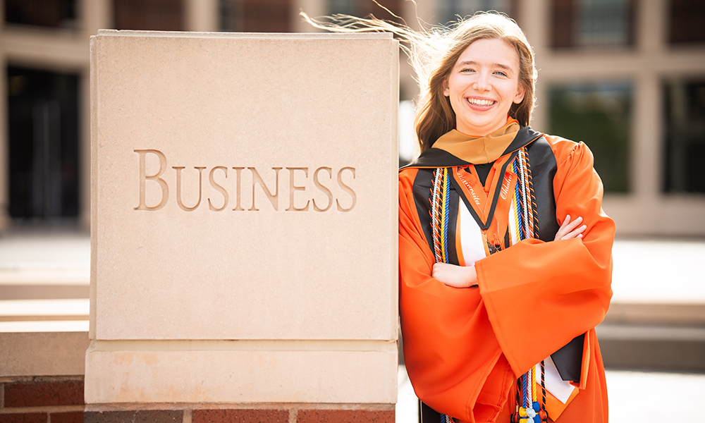 Danielle Nester stands outside the business building and wears her orange gown.
