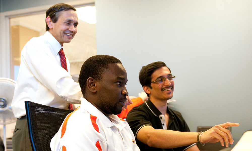 Dr. Sharda and two students look at a computer screen.