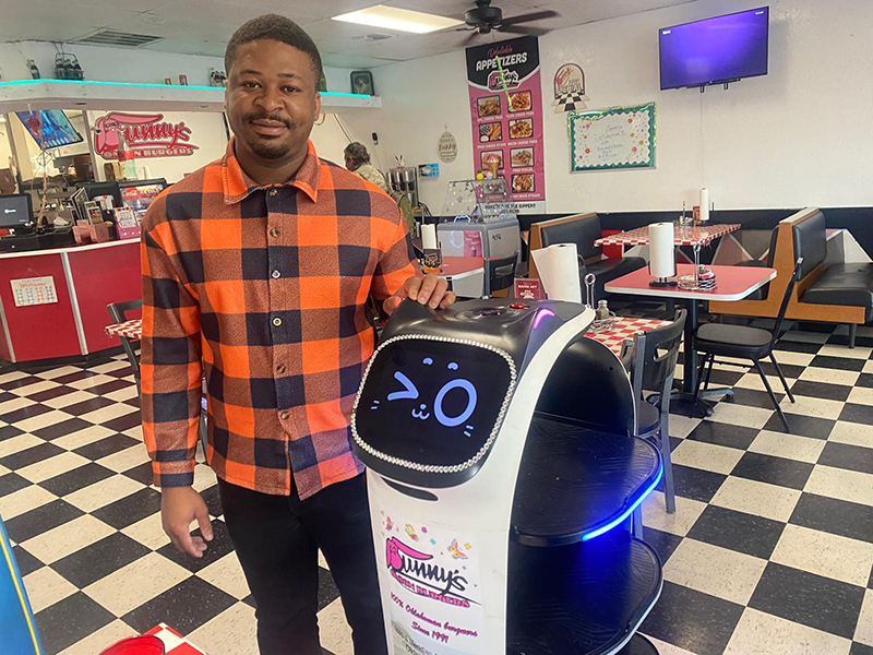 Spears doctoral student Abraham Terrah posing with a robotic waiter at a diner.