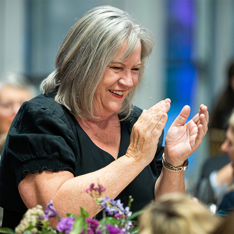 A female Wine Forum guest stands and claps with a big smile on her face.