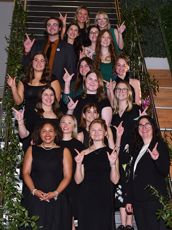 The student chairs of the Wine Forum positioned vertically on a staircase. Each student is holding out their arm in order to do the "Go Pokes" hand sign.