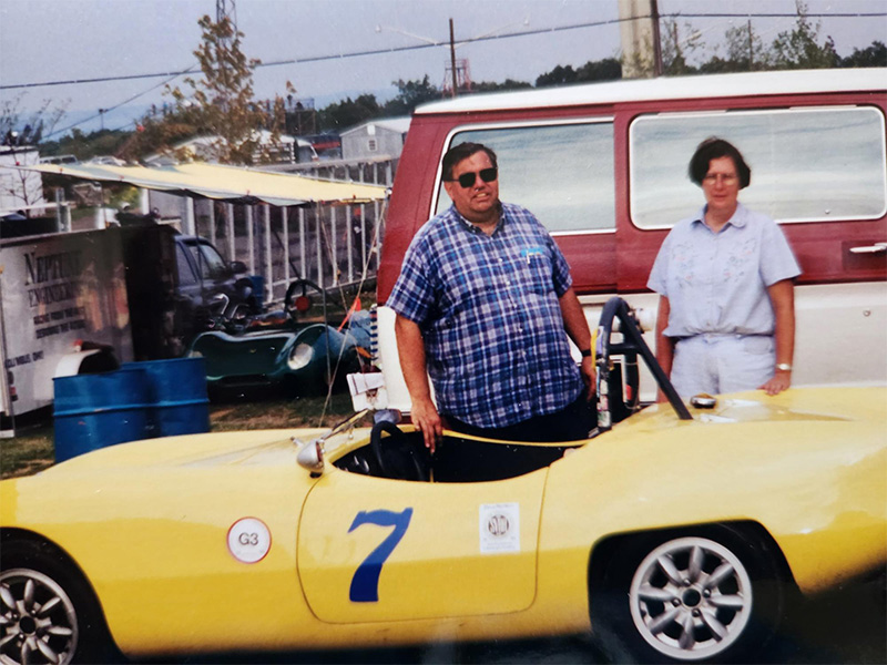A man and woman stand near a yellow racecar.