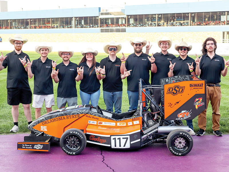A college race team stands behind their racecar at an outdoor track.