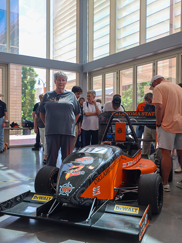 A woman stands inside a modern building with glass walls near a formula race car.