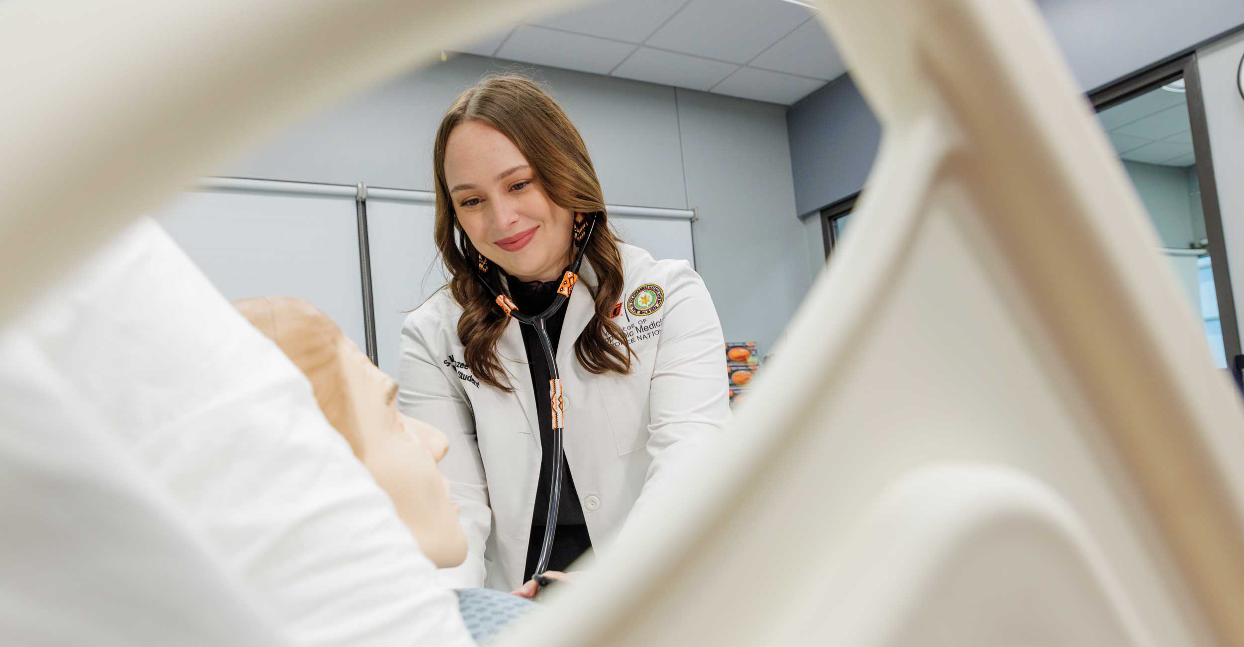 A woman wearing a white coat looks at a medical dummy