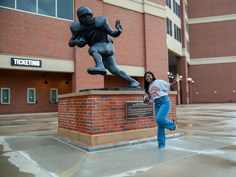 Julicia Thornton A woman does a pose next to a statue of a football player doing the same pose.
