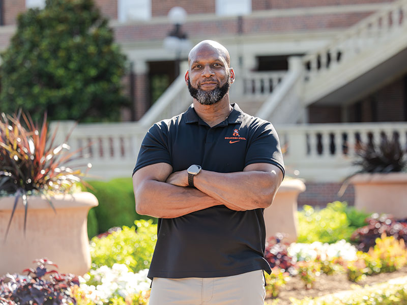 Alton Carter A man stands outdoors with arms crossed, wearing a black polo shirt with an orange logo.
